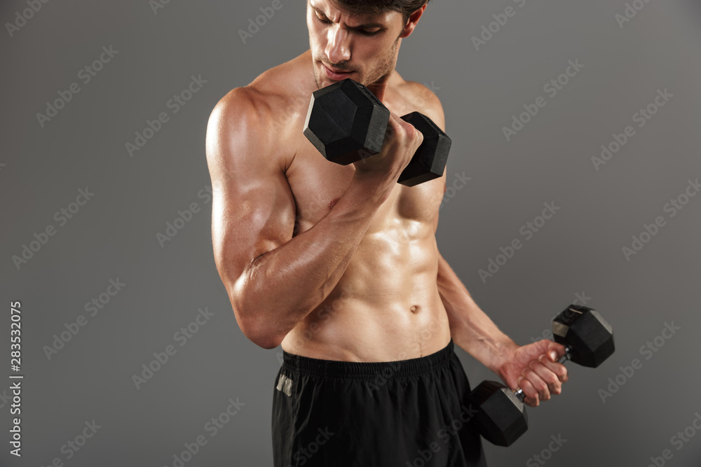 Handsome young strong sportsman posing isolated over grey wall background make exercises with dumbbells for arms.