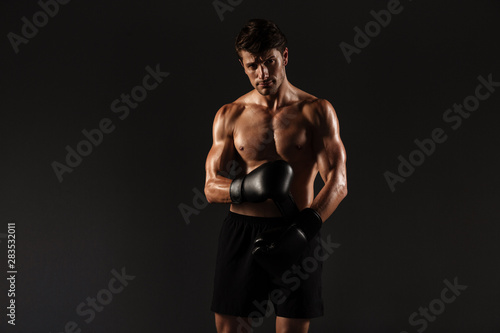 Concentrated strong handsome young sportsman boxer in gloves posing isolated over black wall background.