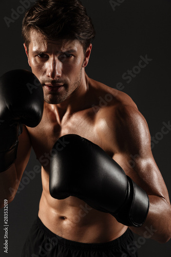 Handsome young strong sportsman boxer in gloves make exercises boxing isolated over black wall background. © Drobot Dean