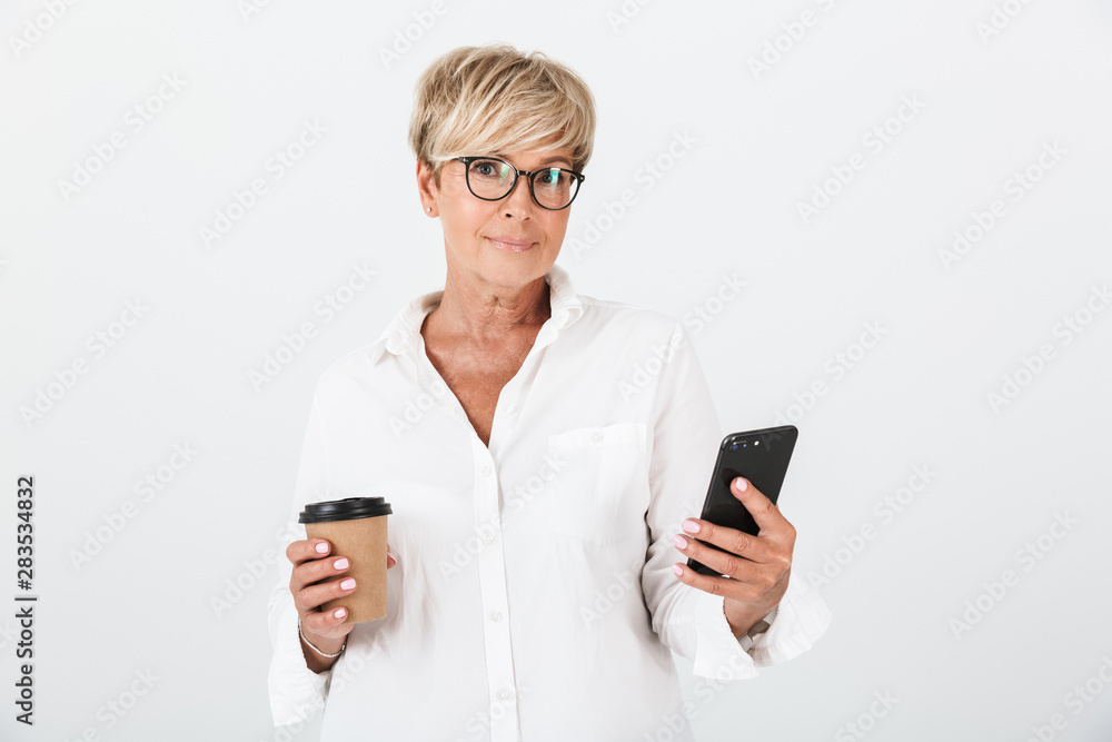 Portrait of caucasian adult woman wearing eyeglasses holding cellphone and takeaway coffee cup