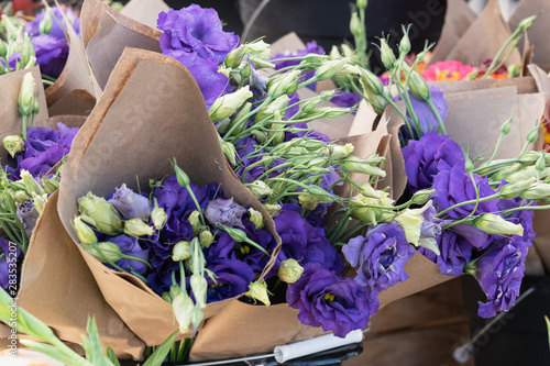 buckets of purple licanthus flowers in bloom and buds wrapped in brown paper at the farmers market photo