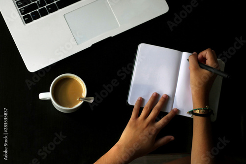 Coffee mug on a desk, with a laptop and a notebook.