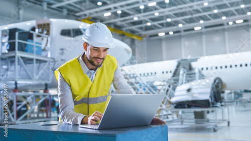 Engineer in Safety vest Working on Computer in Aircraft Maintenance Hangar