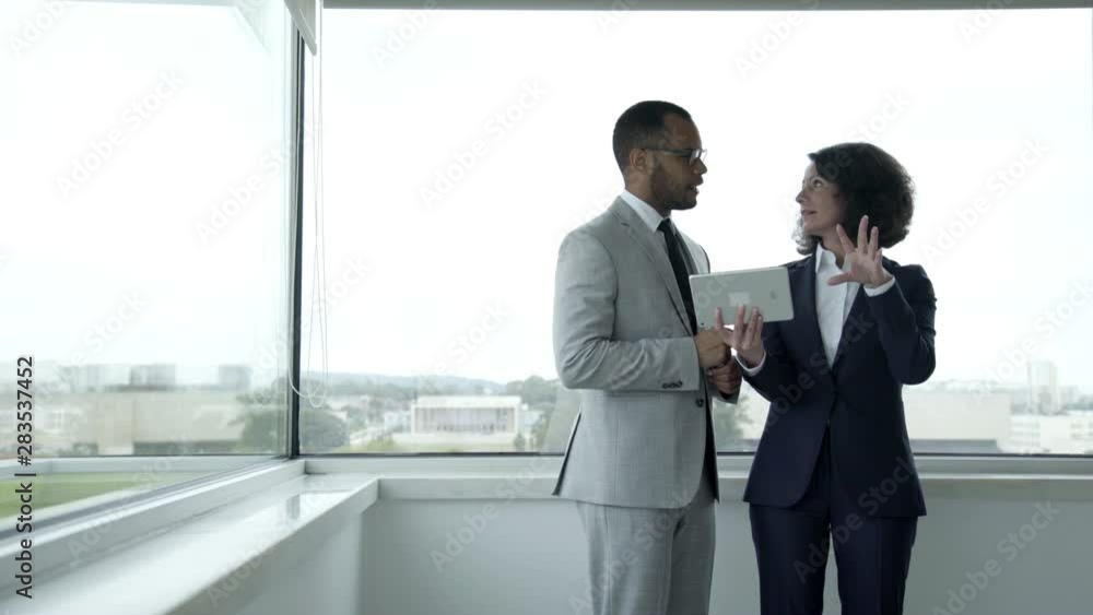Smiling people wearing formal wear using tablet near window. Cheerful colleagues looking at tablet during break. Technology concept Smiling people wearing formal wear using tablet near window. Cheerful colleagues looking at tablet during break. Technology concept