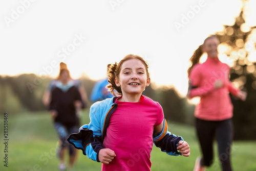 A portrait of small girl with large group of people running in nature.