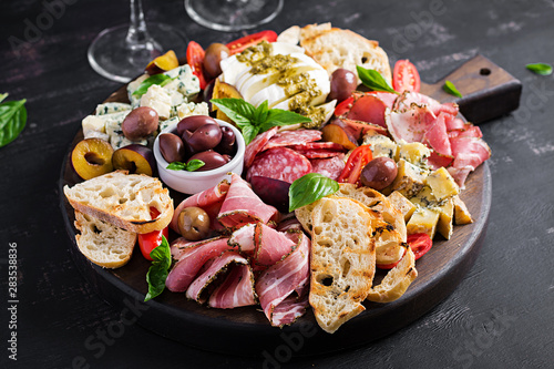 Fotografia Antipasto platter with ham, prosciutto, salami, blue cheese, mozzarella with pesto and olives on a wooden background