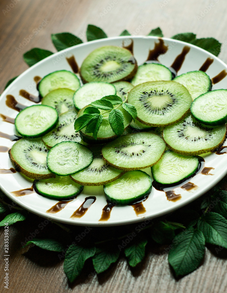 Close-up slices of kiwi and cucumber with leaf on white plate and rustic background Close-up slices of kiwi and cucumber with leaf on white plate and rustic background