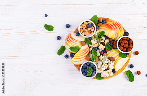 Cheese platter with assorted cheeses, blueberry, apples, nuts on white table. Italian cheese  platter and fruit. Top view, overhead