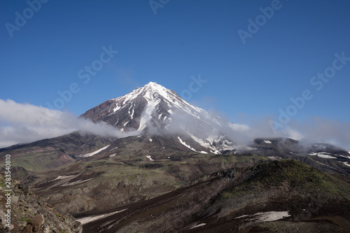 Symmetrical conus of Koryaksky (also known: Koryakskaya Sopka), an active volcano on the Kamchatka Peninsula in the Russian Far East from Avacha base camp. Slopes of volcanic hills in front.