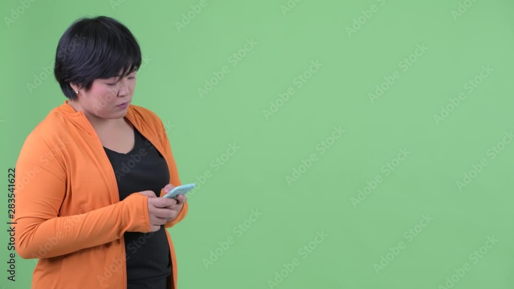 Happy young overweight Asian woman waiting while using phone ready for gym Happy young overweight Asian woman waiting while using phone ready for gym