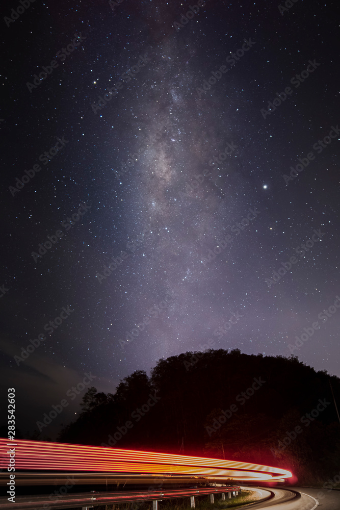 Obraz premium Milky way galaxy with car light trail, stars and space dust in the universe. Long exposure.