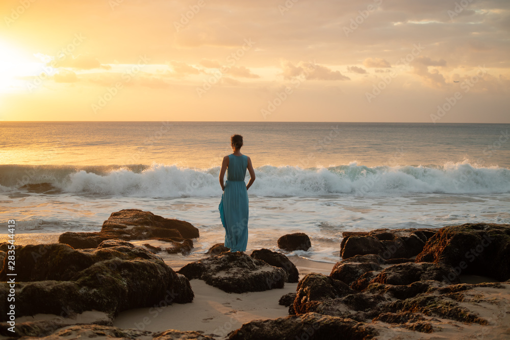 Woman enjoying sunset at the beach. View from back.