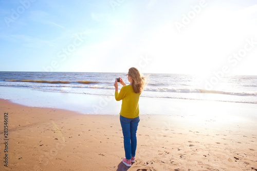 Woman standing on the beach and and take a picture of the sea © sepy