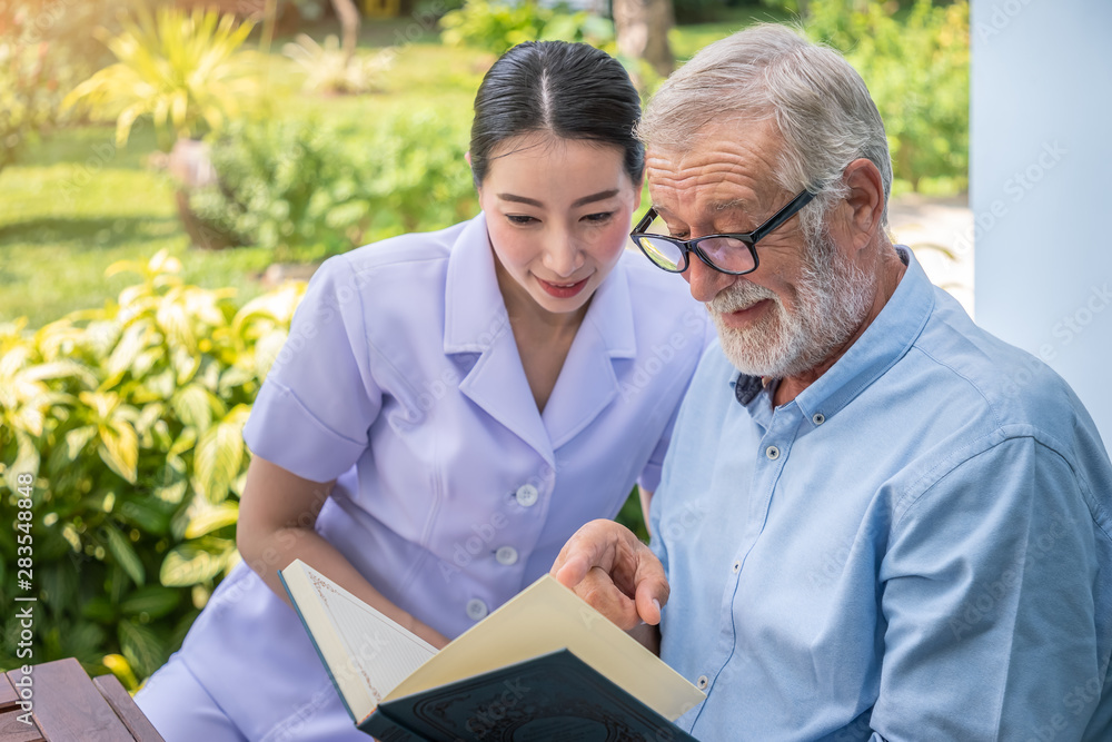 Senior elderly man reading book with nurse during breakfast in garden at nursing home Senior elderly man reading book with nurse during breakfast in garden at nursing home