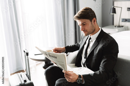 Concentrated serious businessman indoors at home reading newspaper drinking coffee.