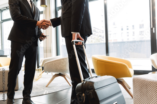 Colleagues indoors in business center office using mobile phone shaking hands.