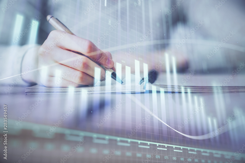 Hands writing information about stock market in notepad. Forex chart holograms in front. Concept of research. Multi exposure Hands writing information about stock market in notepad. Forex chart holograms in front. Concept of research. Multi exposure