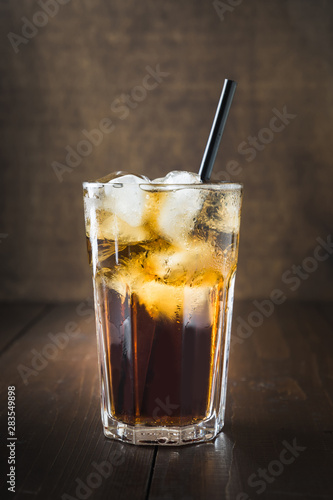 Glass of refreshing drink with ice on dark wooden board.