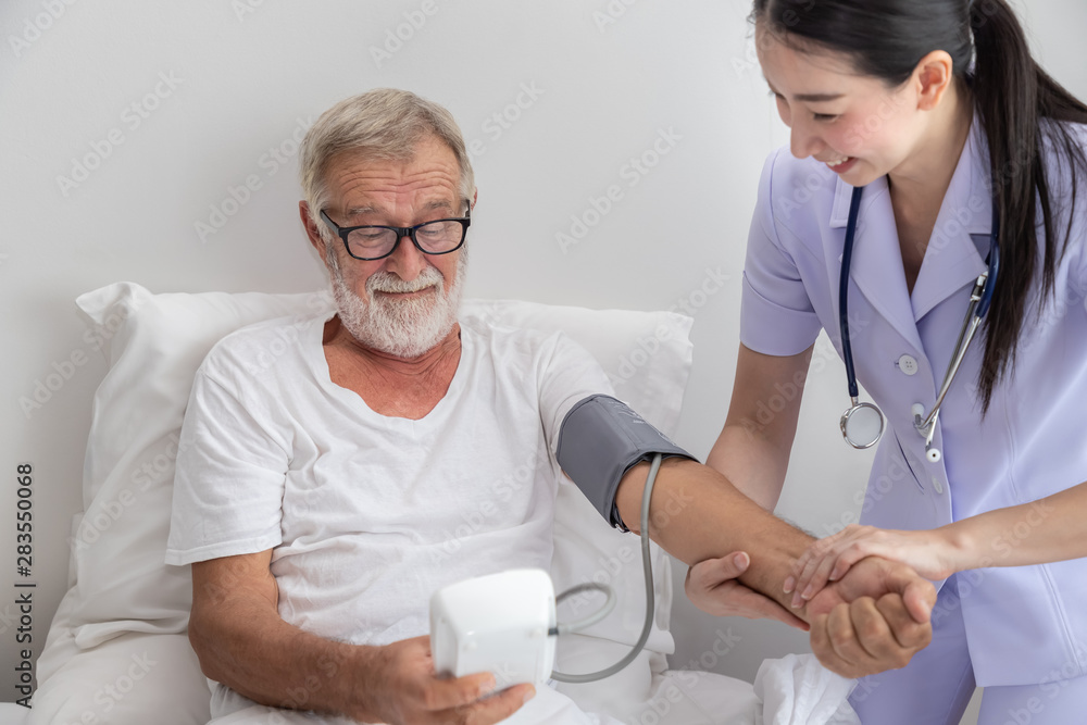 Happy nurse checking and measuring elderly man blood pressure with device in bedroom at nursing home Happy nurse checking and measuring elderly man blood pressure with device in bedroom at nursing home