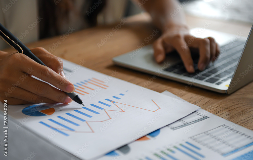 Female businessmen point the pen at the data graph and use the laptop to work. Female businessmen point the pen at the data graph and use the laptop to work.