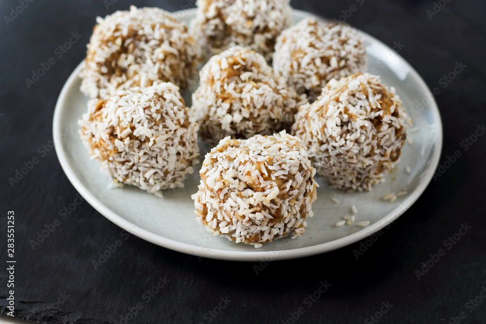 vegetarian raw healthy diet no bake candies balls dessert sweets sugar free gluten-free with coconut flakes, proper nutrition snack on blue plate and black slate background, soft selective focus vegetarian raw healthy diet no bake candies balls dessert sweets sugar free gluten-free with coconut flakes, proper nutrition snack on blue plate and black slate background, soft selective focus