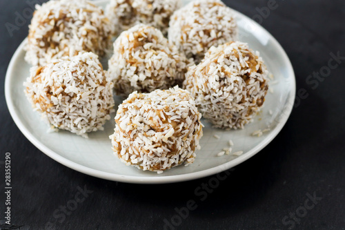 vegetarian raw healthy diet  no bake candies balls dessert sweets sugar free gluten-free with coconut flakes, proper nutrition snack on blue plate and black slate background, soft selective focus