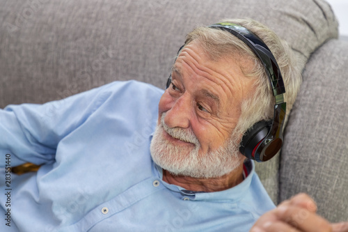 Senior old man eldery enjoy listening to music with headphone on couch sofa