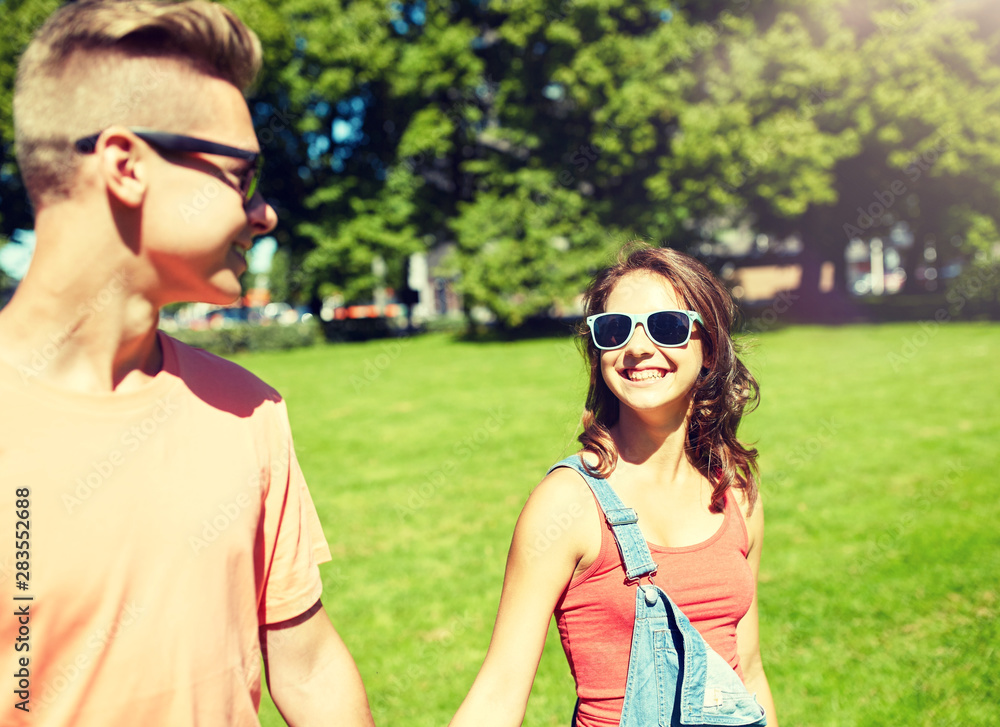 holidays, vacation, love and people concept - happy smiling teenage couple walking and looking at each other in summer park holidays, vacation, love and people concept - happy smiling teenage couple walking and looking at each other in summer park