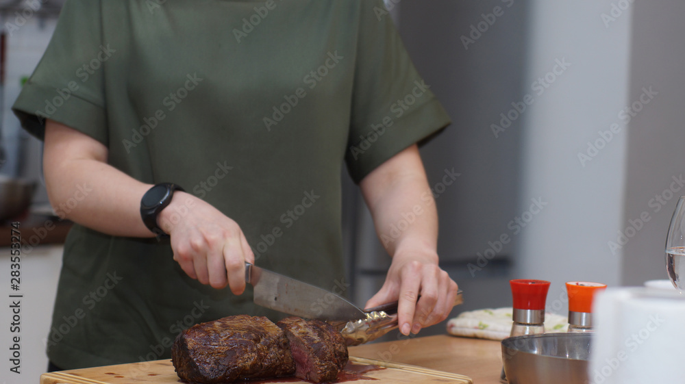 A cook with a round clock slices a baked beef tenderloin on a wooden board