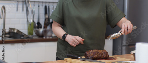 A cook with a round clock takes a beef tenderloin with tongs