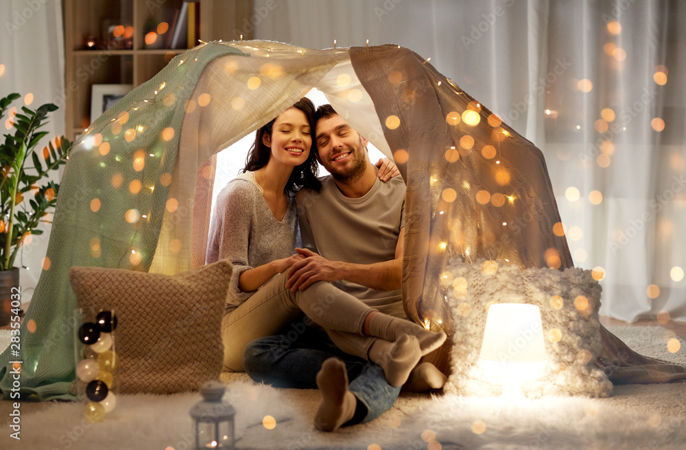 leisure, hygge and people concept - happy couple in kids tent at home