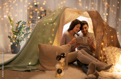 leisure, hygge and people concept - happy couple drinking coffee or tea in kids tent at home photo