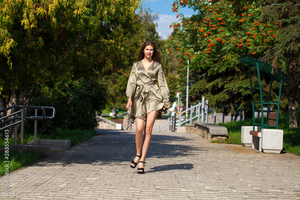 Fototapeta premium Young beautiful woman in green dress walking on the summer street