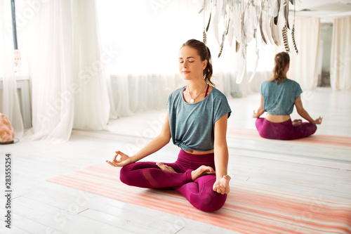 mindfulness, spirituality and healthy lifestyle concept - woman meditating in lotus pose at yoga studio photo