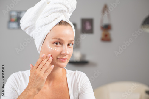 Happy young woman applying cream to her face. Woman face skin care.