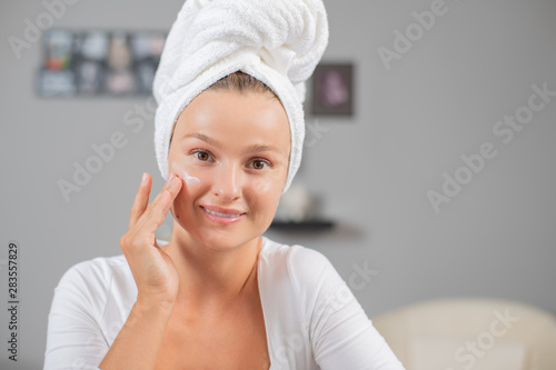 Happy young woman applying cream to her face. Woman face skin care.