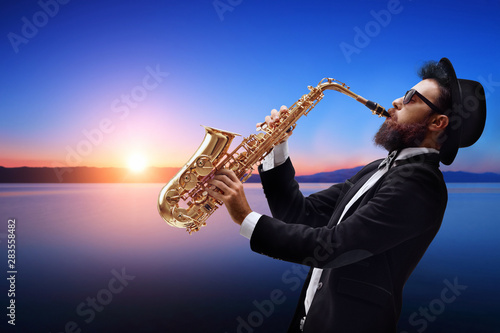 Male jazz musician playing a saxophone with a sunset and water