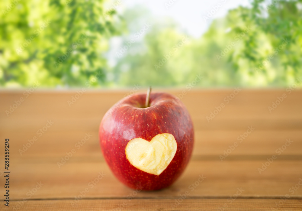 fruits, food and health concept - ripe red apple with carved heart shape on wooden table over green natural background fruits, food and health concept - ripe red apple with carved heart shape on wooden table over green natural background