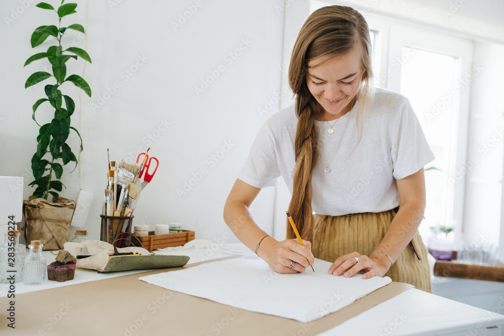 Young woman artist drawing on sheet, behind the table at home.