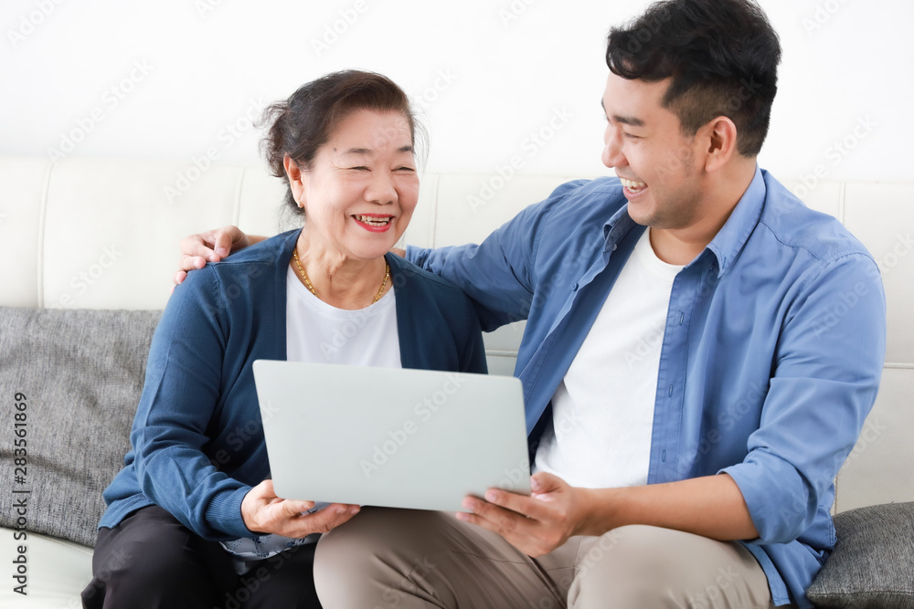 Asian young man and senior woman using laptop computer in living room concept Son teach mother use computer laptop Asian young man and senior woman using laptop computer in living room concept Son teach mother use computer laptop
