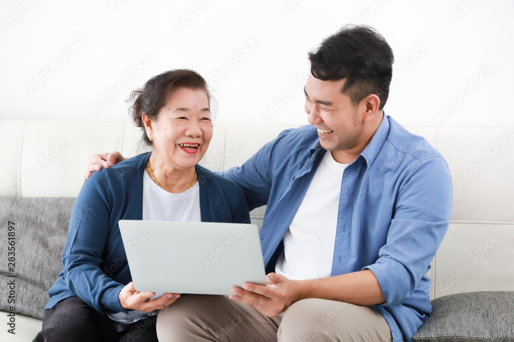 Asian young man and senior woman using laptop computer in living room concept Son teach mother use computer laptop Asian young man and senior woman using laptop computer in living room concept Son teach mother use computer laptop