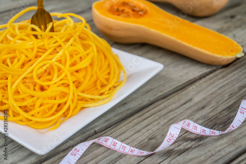 Butternut squash noodles with fork and measuring tape on wooden background.