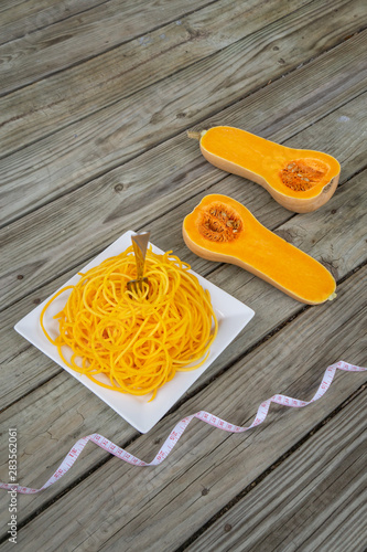 Butternut squash noodles with fork and measuring tape on wooden background.