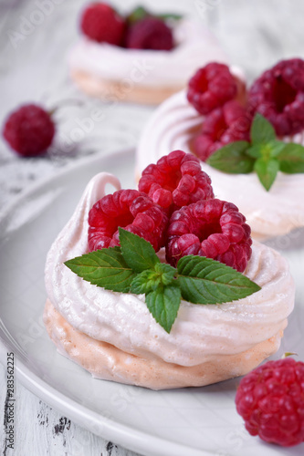 Mini Pavlova cakes topped with raspberries and mint on white wooden table