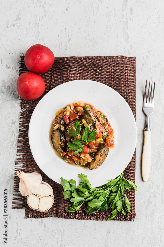 Summer salad of eggplant and tomato on a white plate on a light background