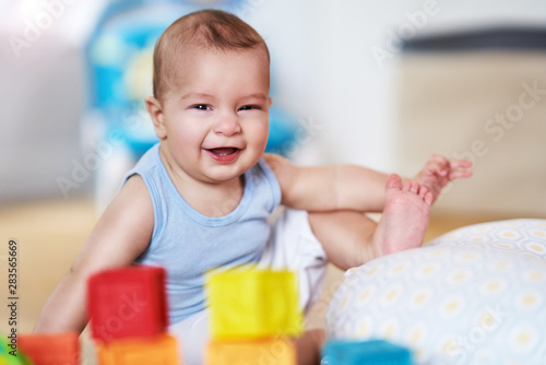 Cute smiling baby boy sitting on floor in living room