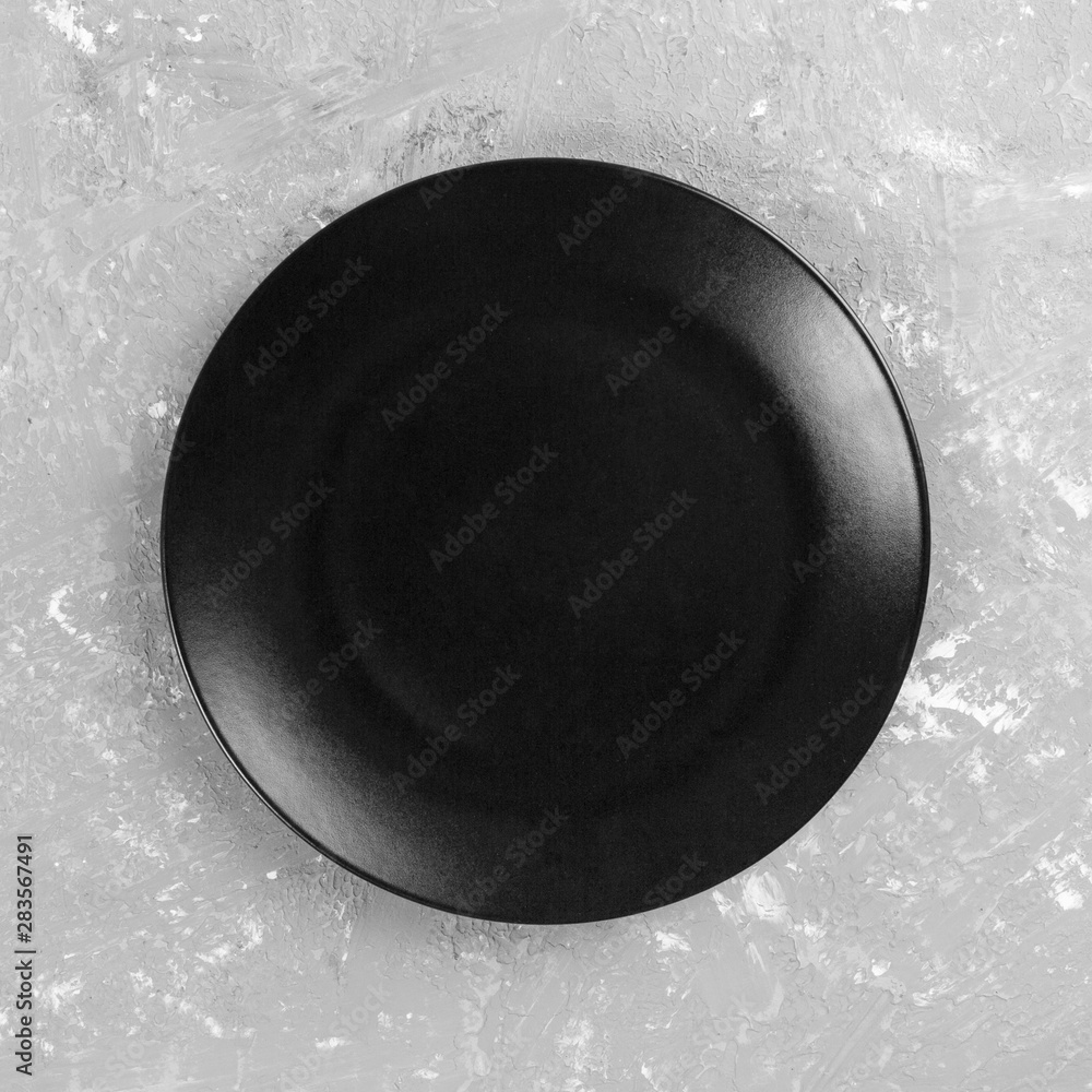 Black round plate on gray cement background, top view, copy space