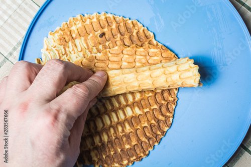 Male hand twists thin waffles into straw on round lid.