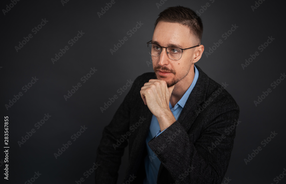 Studio portrait of a pensive young man in glasses with a beard on a dark background. Studio portrait of a pensive young man in glasses with a beard on a dark background.
