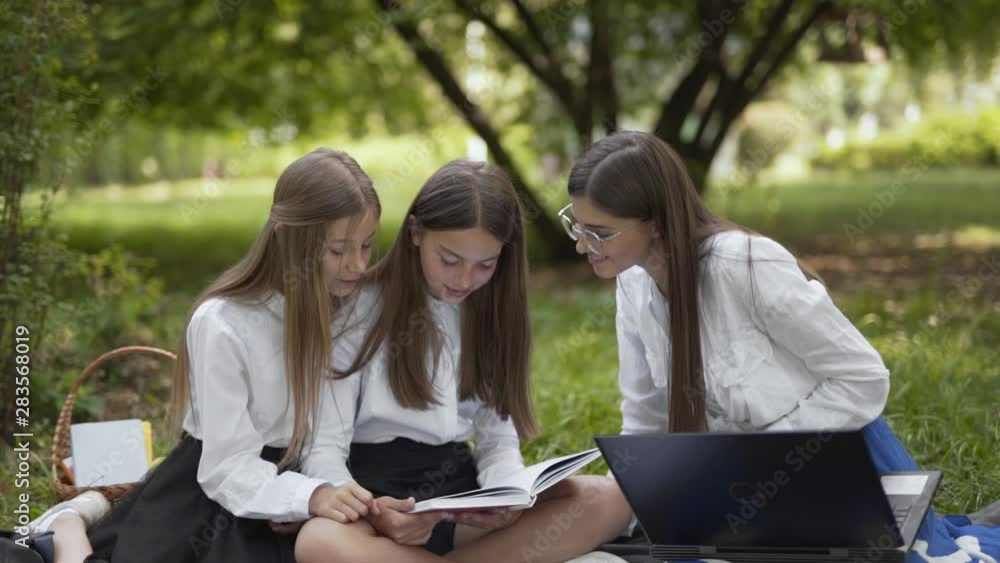 Polish daughters learning to read under guidance of their mother at a park, medium shot Polish daughters learning to read under guidance of their mother at a park, medium shot